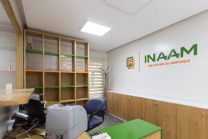 Bureau du projet Inaam avec une étagère en bois, logo d'Inaam sur le mur, et des accents colorés en vert et orange pour une atmosphère professionnelle et accueillante.