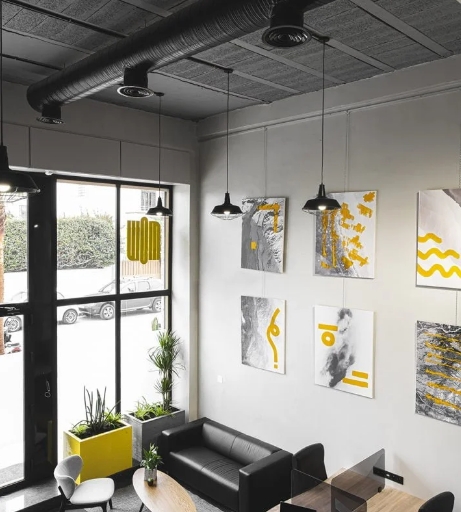 Vue intérieure d’un espace de coworking au style industriel, avec des œuvres d’art abstrait accrochées aux murs et un mobilier moderne.