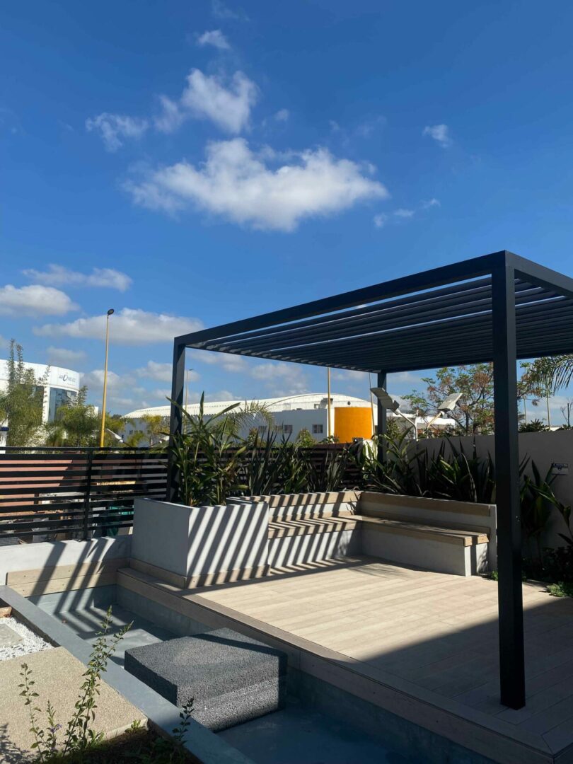 Terrasse extérieure moderne avec une pergola en métal, des plantes et un mobilier de jardin épuré, offrant un espace de détente en plein air.