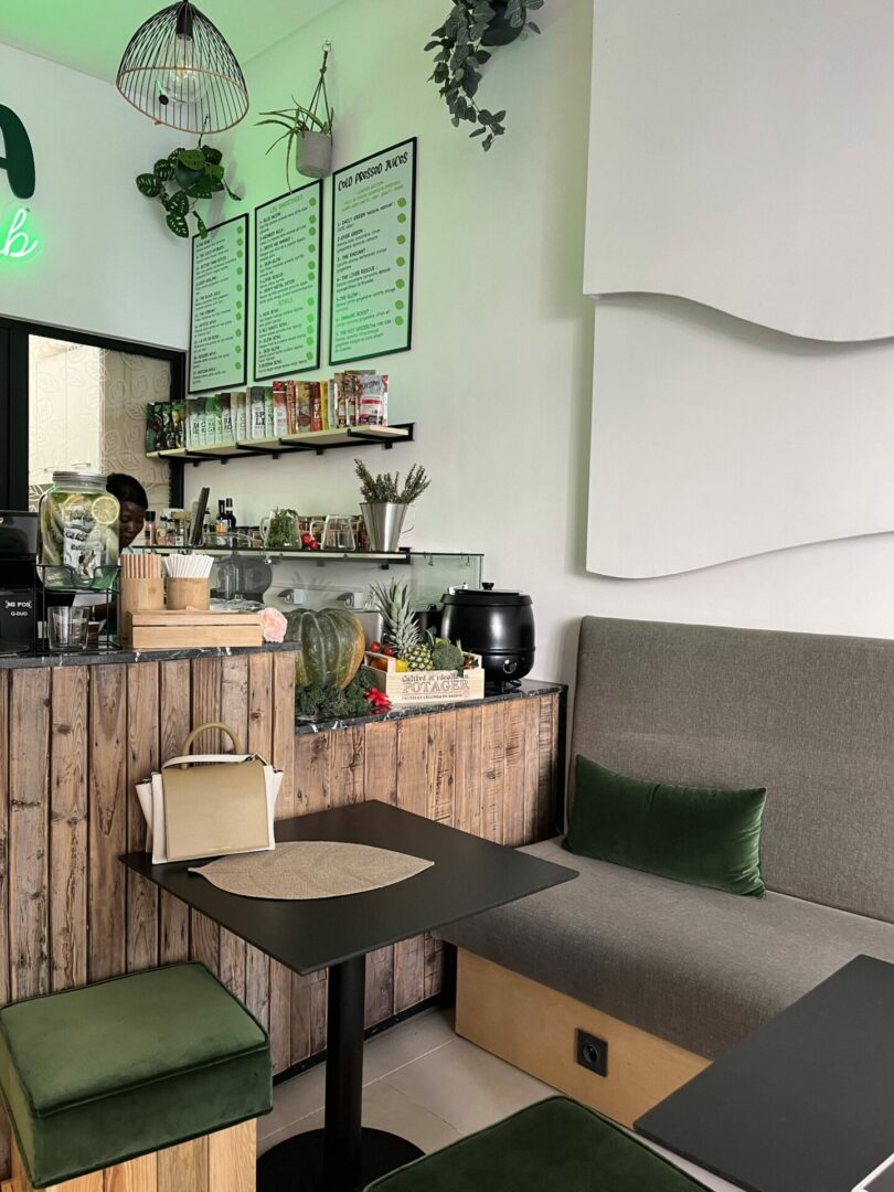 Coin cosy d’un café avec une décoration bohème chic, combinant des éléments en bois, des plantes suspendues et un mobilier en velours vert pour une ambiance chaleureuse