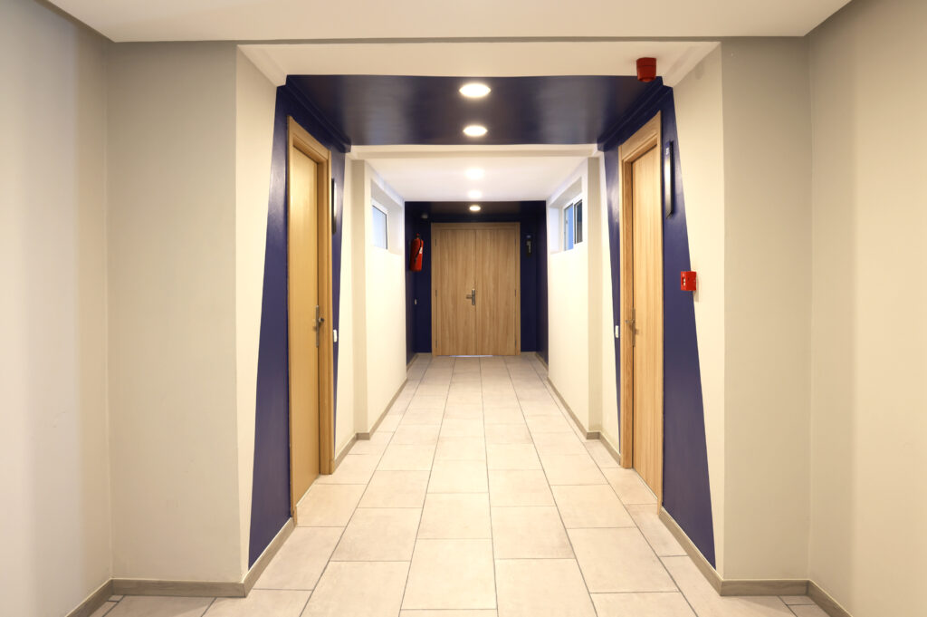 Vue d'un couloir avec des portes de salles en bois et un plafond bleu dans une école de design