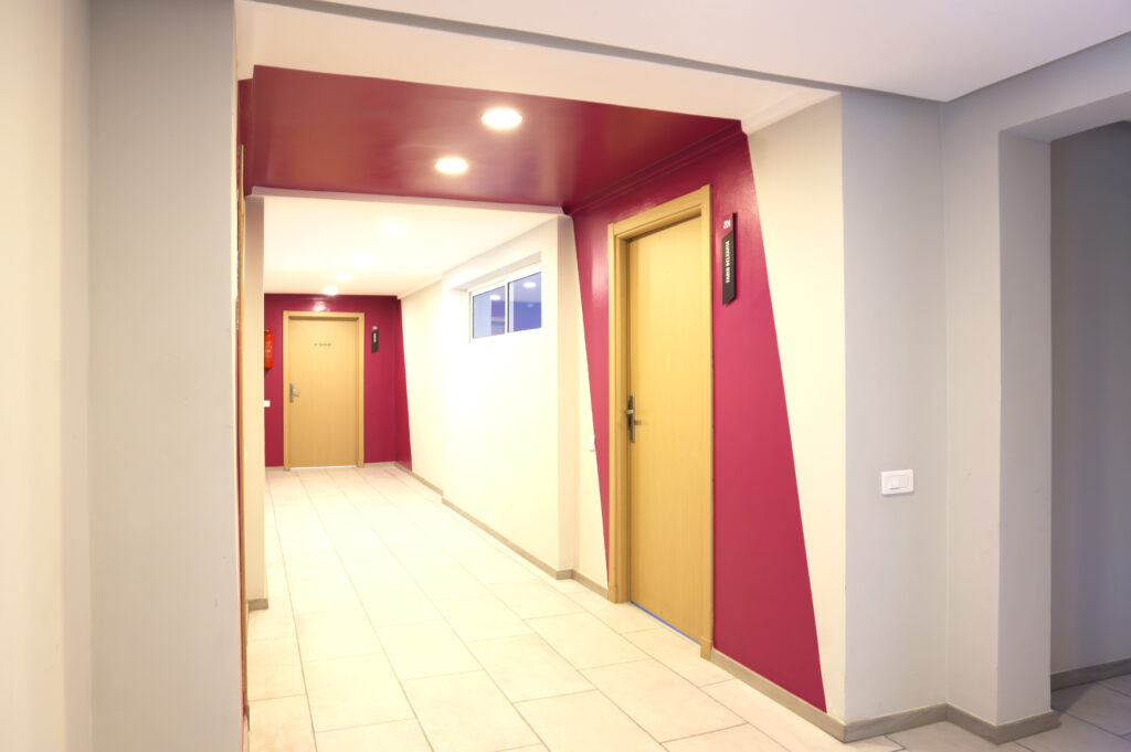 Couloir lumineux d'une école de design avec des portes signalées par des noms, sur des murs aux couleurs vives