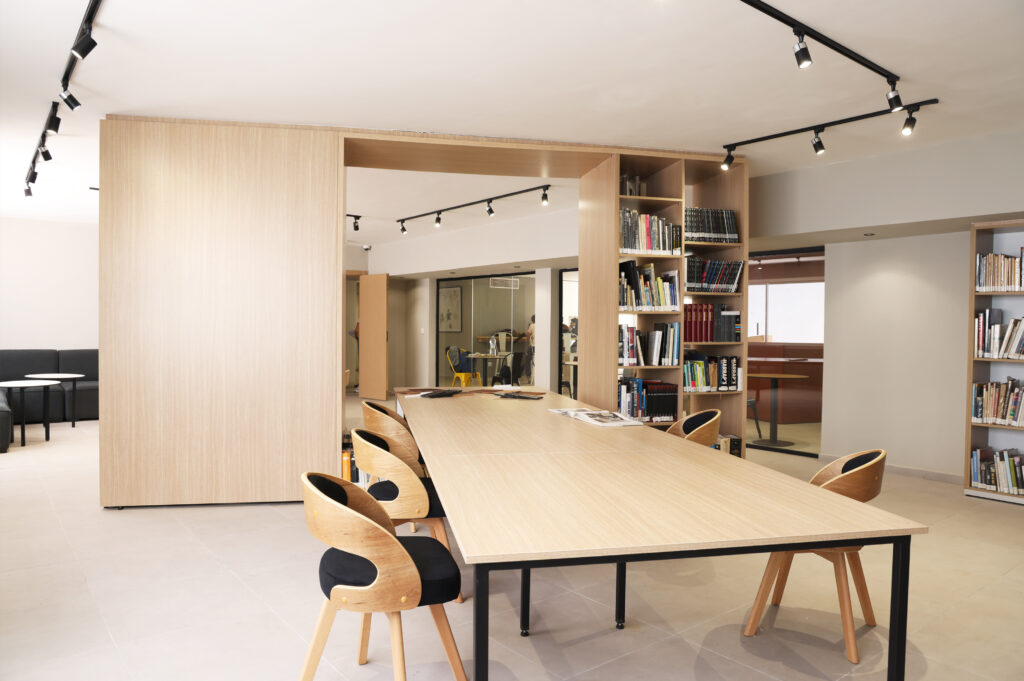 Vue de l'intérieur d'une salle de réunion à Art'ComSup, présentant une grande table en bois, des chaises confortables, et des étagères remplies de livres, créant un environnement propice à l'apprentissage et à la collaboration