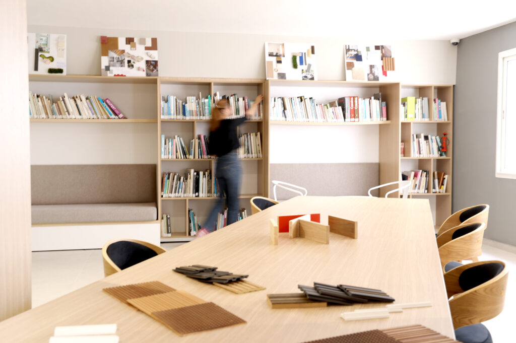 Une étudiante range des livres dans une bibliothèque à Art'ComSup, mettant en valeur un espace de travail lumineux et moderne avec une grande table et des chaises confortables