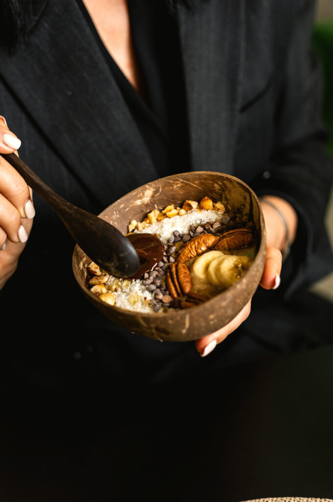 Personne dégustant un bol d'açaï garni de bananes, noix, et pépites de chocolat chez GAIA Juice