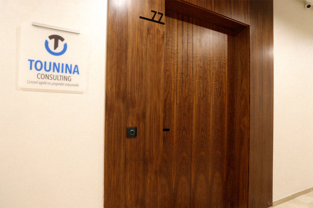 Panneau en relief avec le logo de Tounina Consulting, affichant le nom de la société et un message indiquant 'Conseil agréé en propriété industrielle', situé à côté d'une porte en bois, marquée du numéro de bureau 77