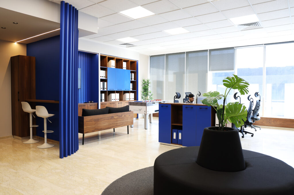 Intérieur du bureau chez Tounina Consulting, mettant en avant un canapé moderne, un mur bleu avec télévision, et des rangements élégants pour documents, accompagné d'une table de baby-foot