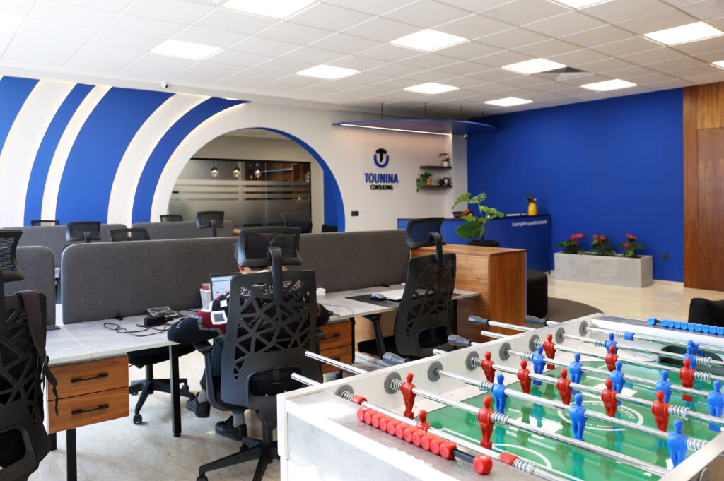 Vue de l'intérieur du bureau Tounina Consulting, mettant en avant un espace de travail avec des bureaux modernes, un design mural bleu, et une table de baby-foot en avant-plan