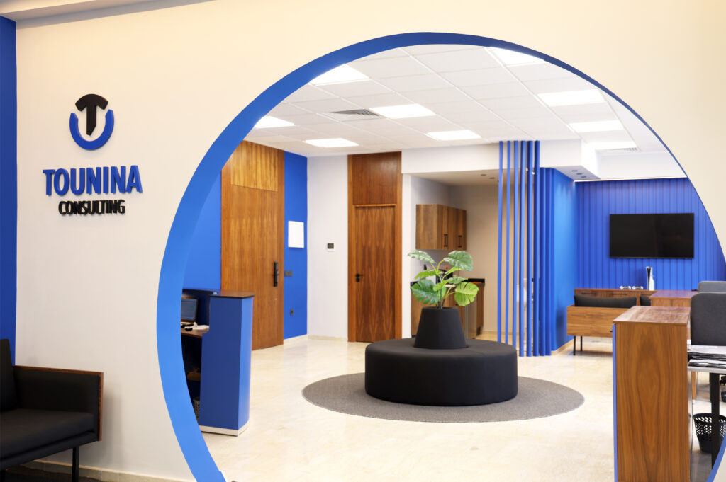 Entrée moderne de Tounina Consulting, mettant en avant le logo de l'entreprise sur un mur bleu, un coin salon avec canapé, et une décoration de plante au centre